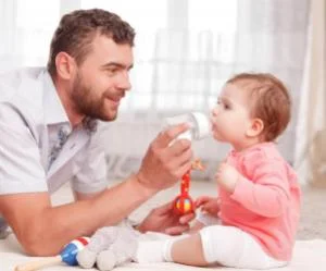 papa-donne-biberon-bébé-fille-1-an-assis